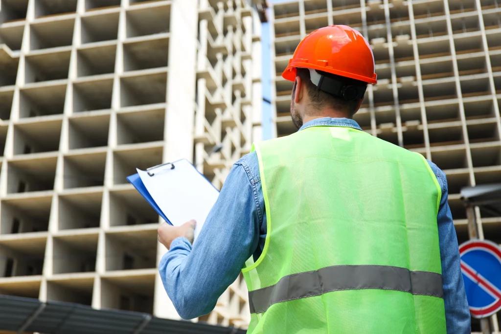 civil-engineer-safety-hat-with-clipboard-against-construction