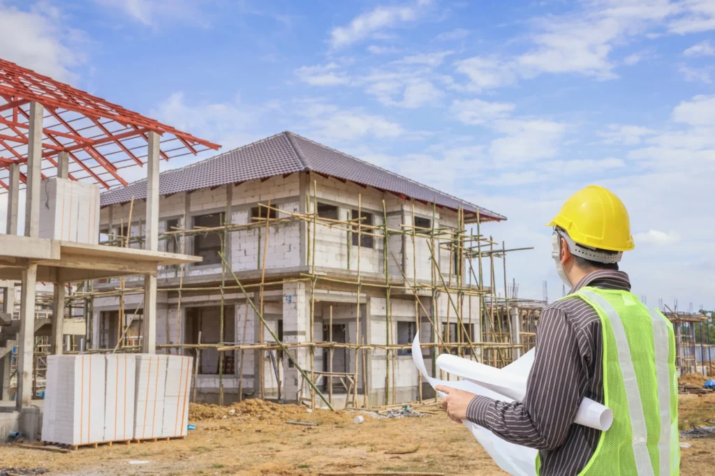 Professional engineer and architect at house construction site with blueprints and protective helmet
